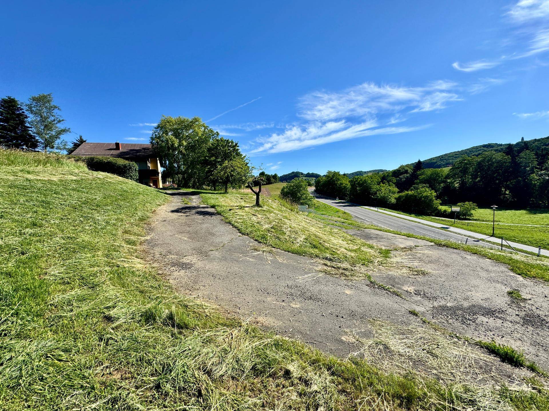 Weitläufige Zufahrt mit Blick auf das Haus und die umliegende grüne Hügellandschaft.