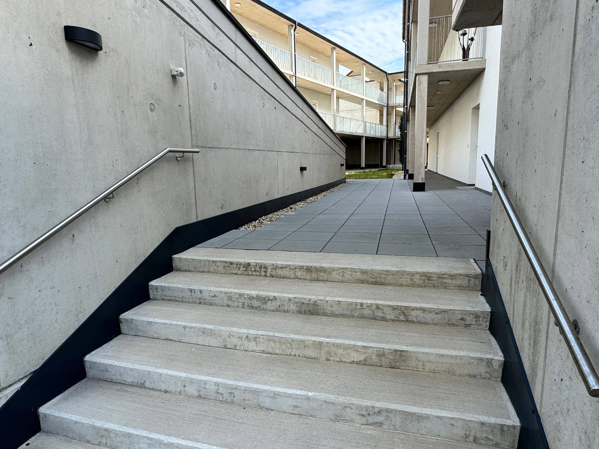 Außentreppe und Zugangsbereich zu den Wohnungen in einem modernen Komplex, mit Handläufen.
