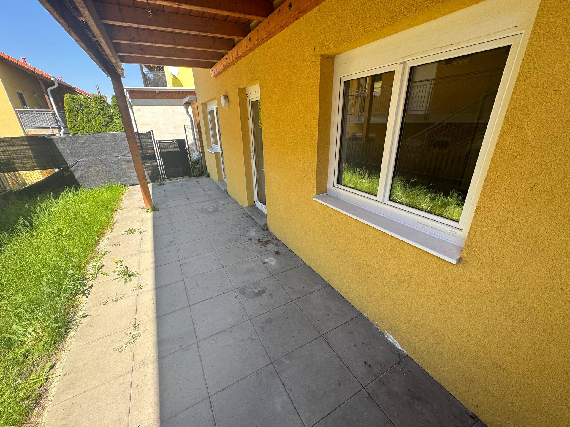 Gepflasterte Terrasse entlang der gelben Hauswand mit Fenstern und Zugangstüren.