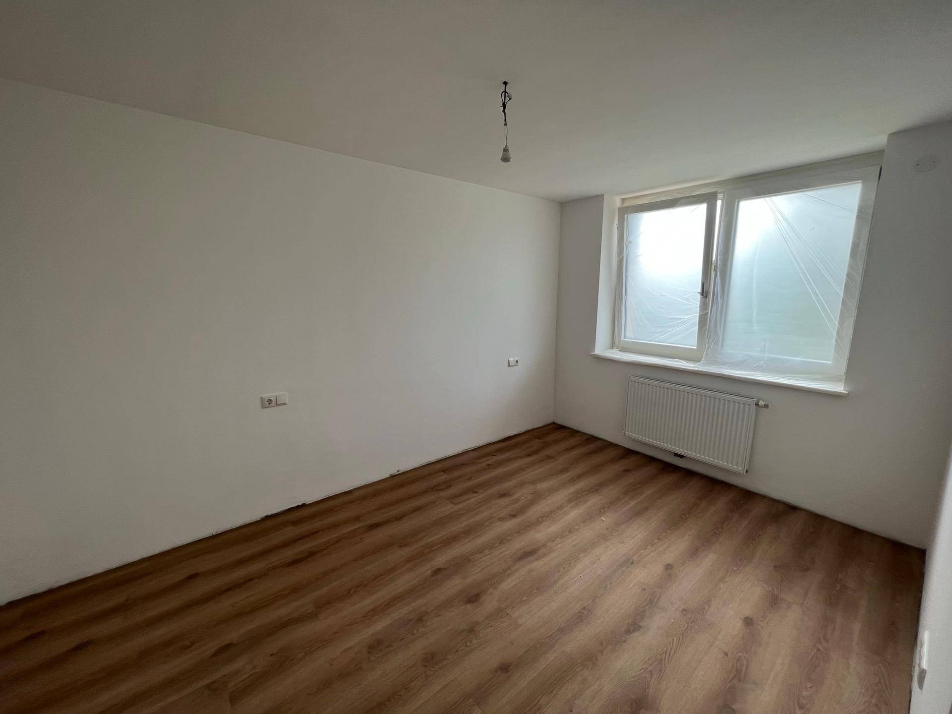 Helles Schlafzimmer mit Laminatboden und großem Fenster, bereit für die Einrichtung.