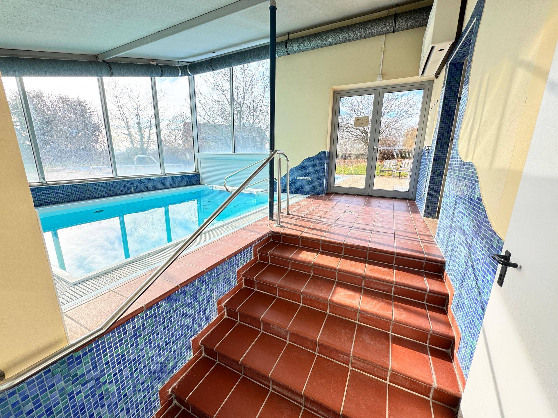 Innenpoolbereich mit Treppe zum Pool und großen Fenstern.