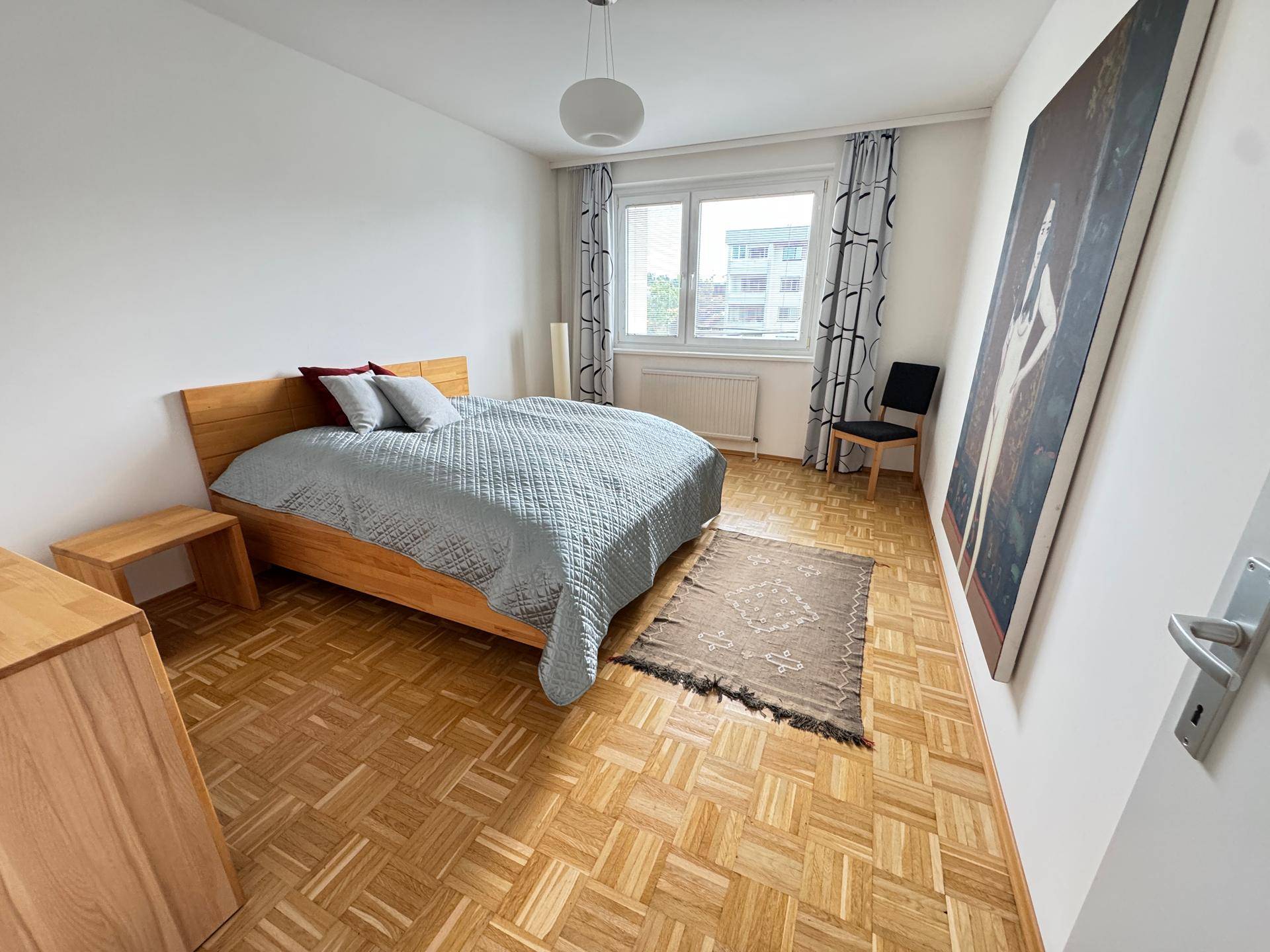 Helles Schlafzimmer mit Parkettboden, Holzmöbeln und großem Fenster für viel Tageslicht.