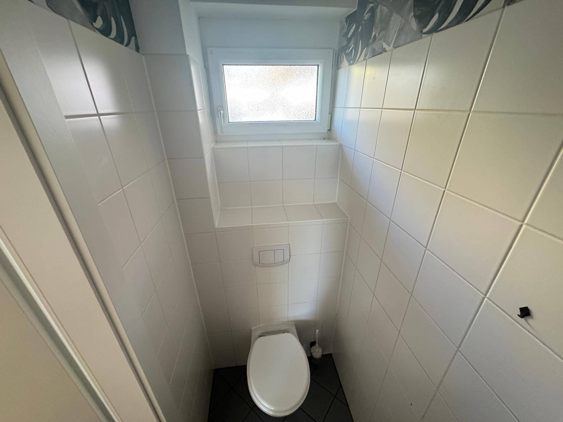 Kleines WC mit weißen Fliesen, wandhängender Toilette und Fenster für natürliche Belüftung.