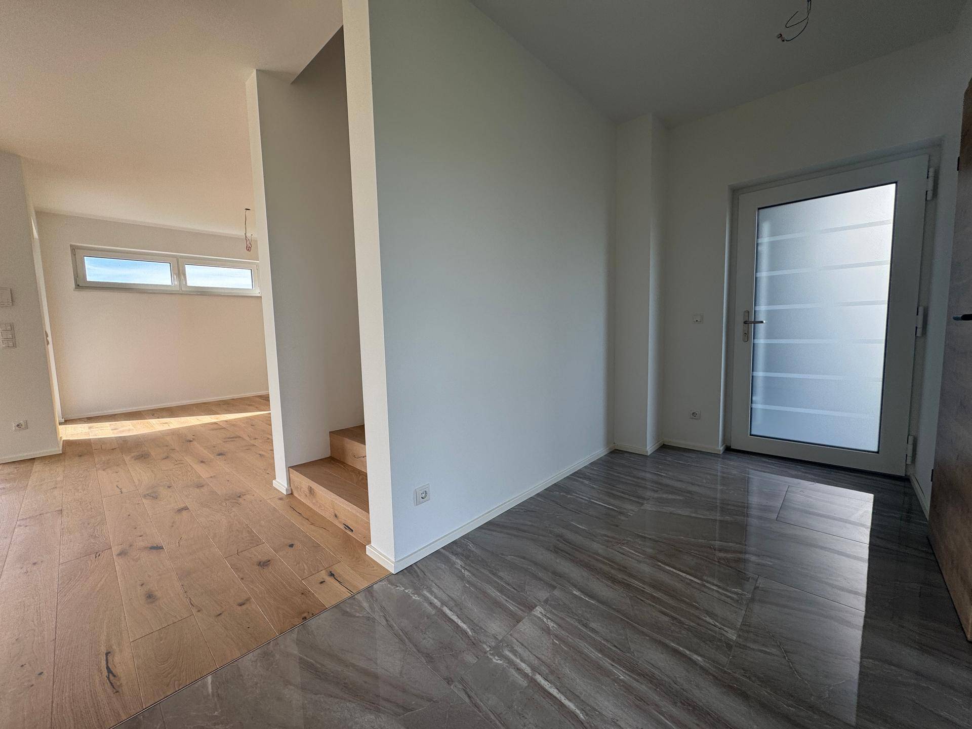 Übergangsbereich zwischen gefliestem Eingang und Wohnbereich mit Eichenparkett und Treppe.