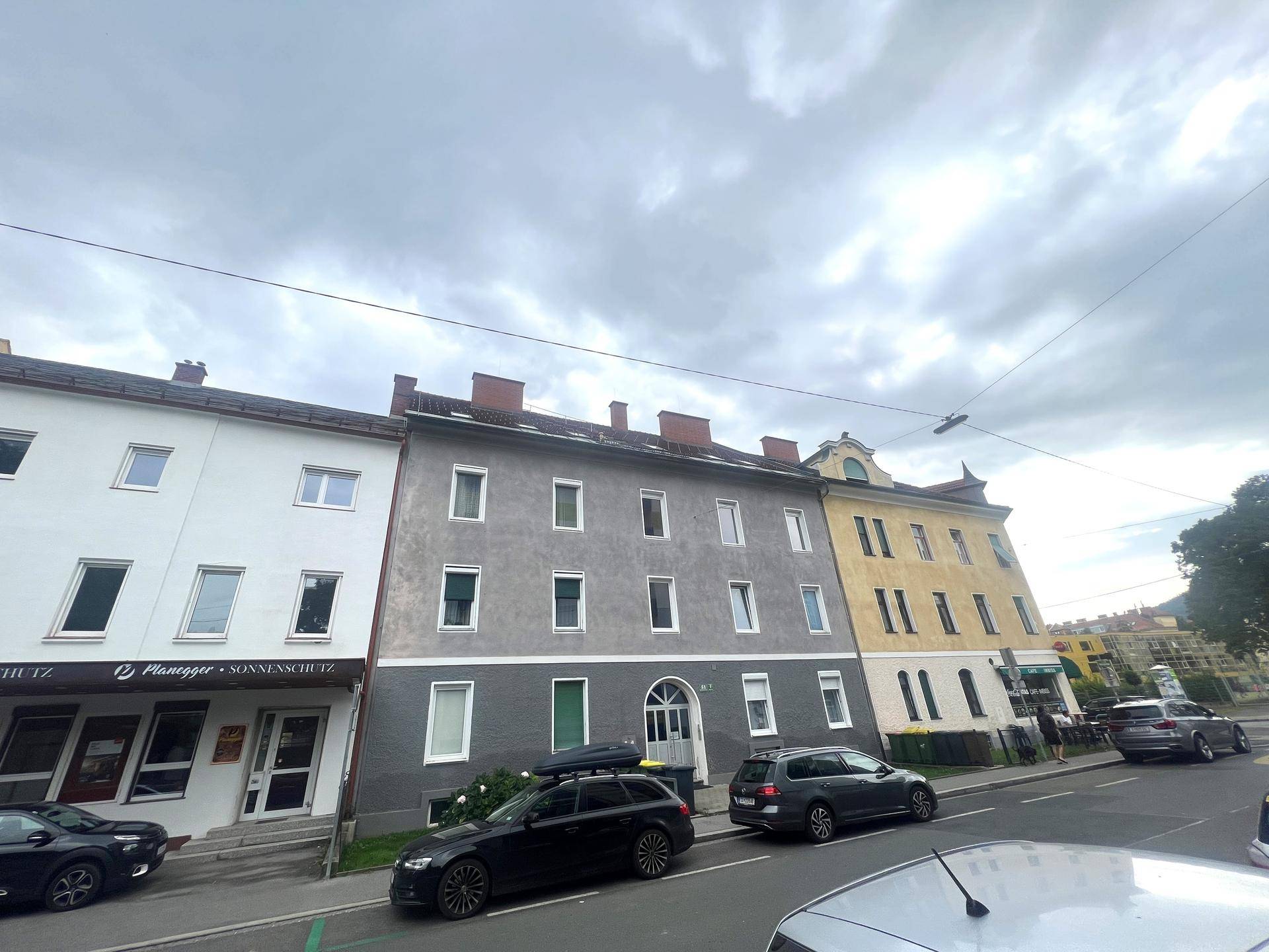 Mehrfamilienhaus mit grauer Fassade und mehreren Fenstern an einer städtischen Straße.