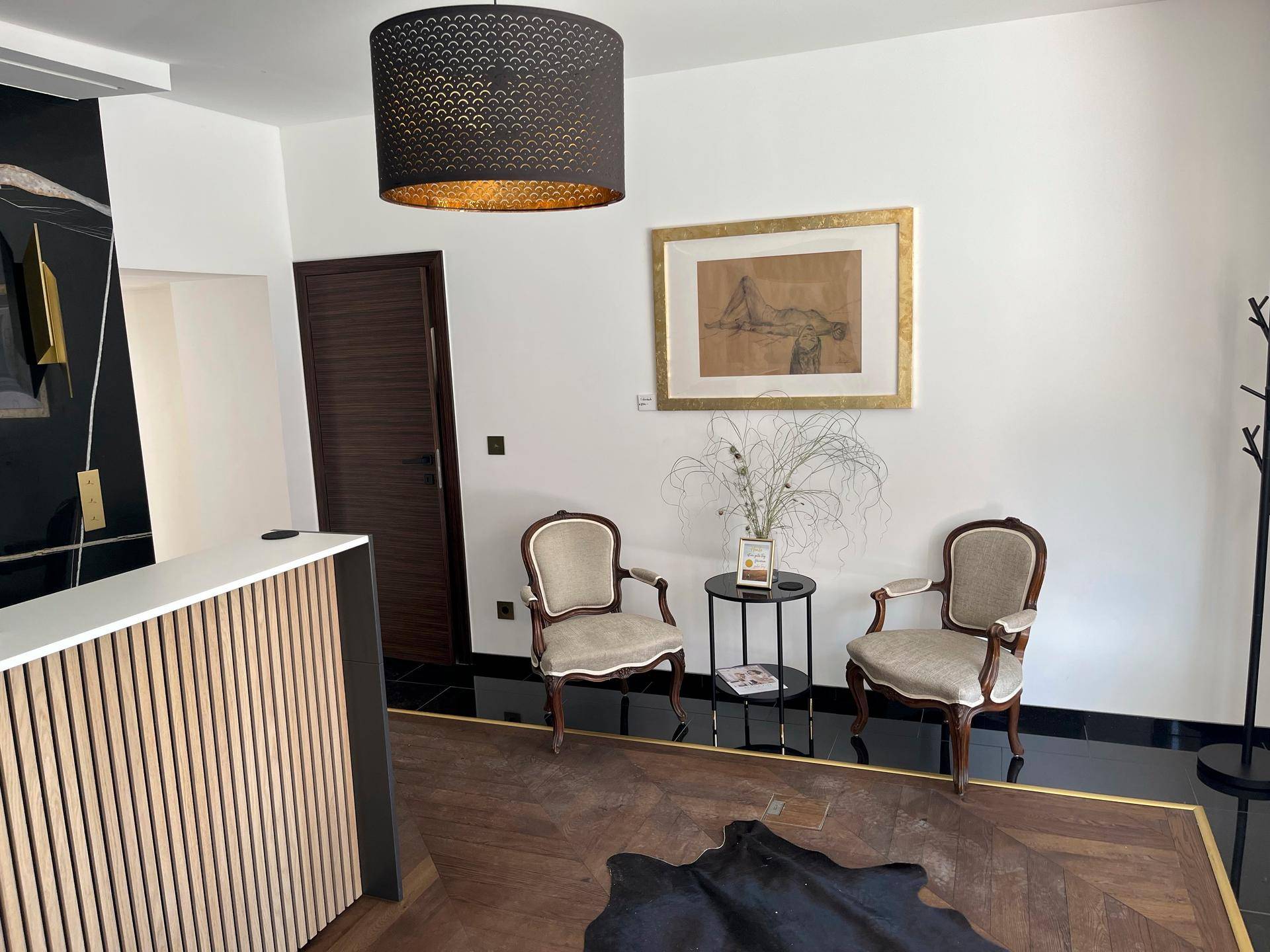 Gemütlicher Wartebereich mit zwei klassischen Sesseln, einem Beistelltisch und Kunst an der Wand.