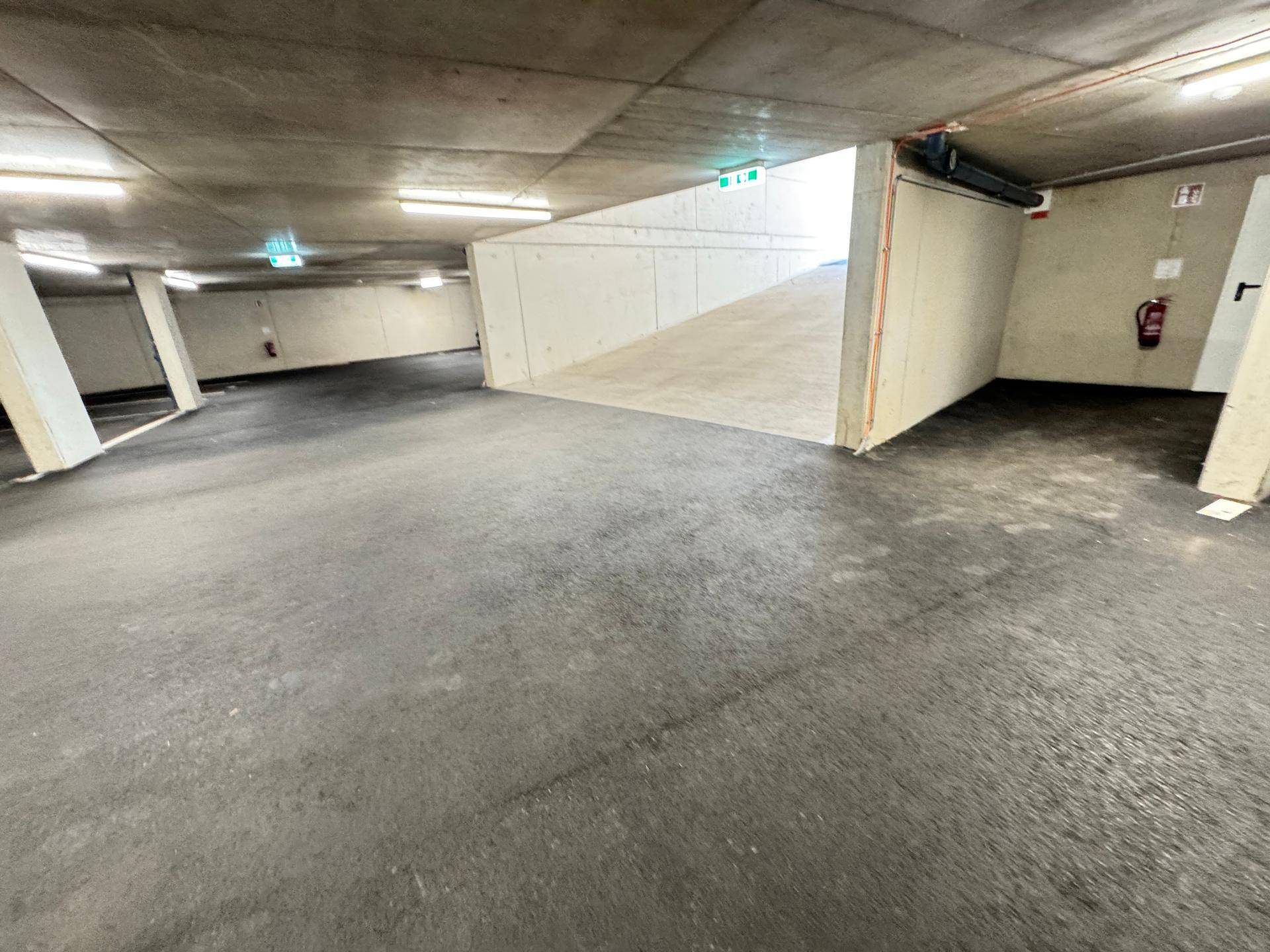 Geräumige Tiefgarage mit Betonwänden und -decken, gut beleuchtet.
