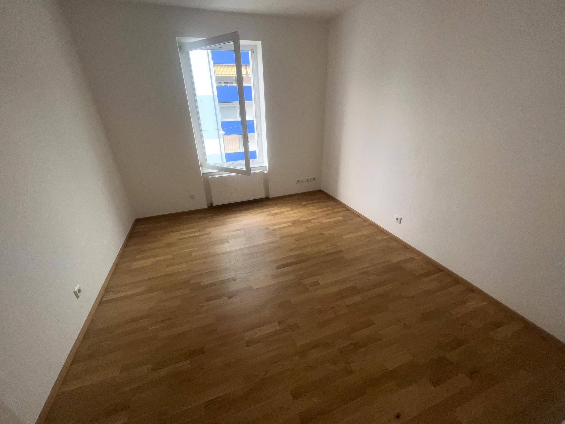 Geräumiges Schlafzimmer mit Parkettboden und einem großen Fenster für viel Tageslicht.