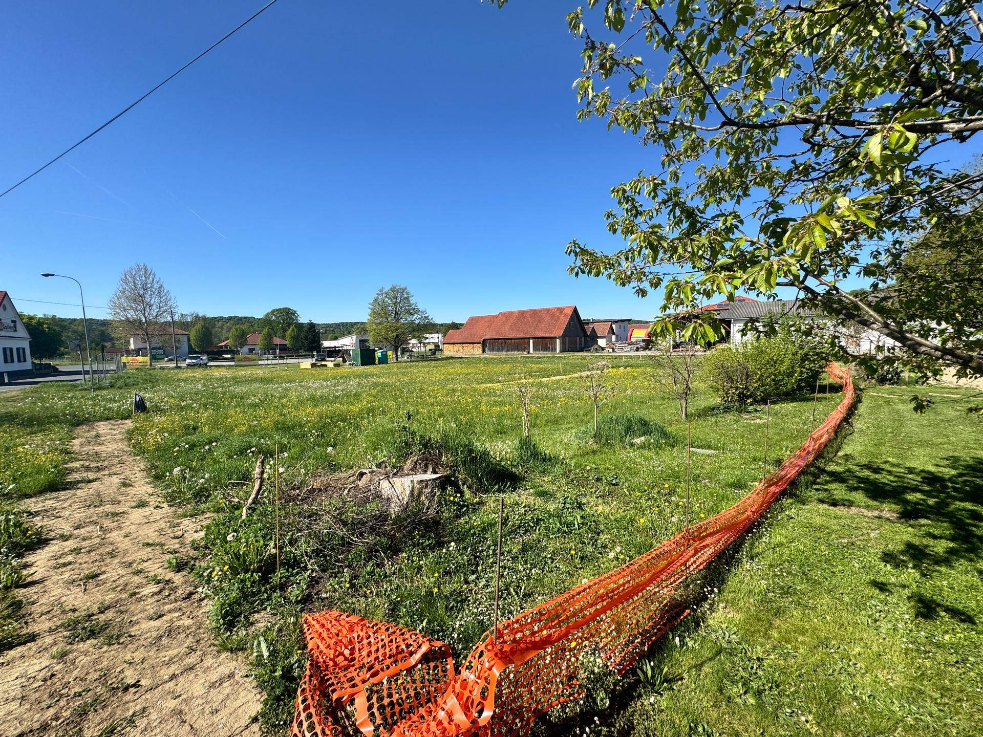 Grünes Grundstück mit Bauzaun im Vordergrund und Blick auf die ländliche Umgebung und Häuser.