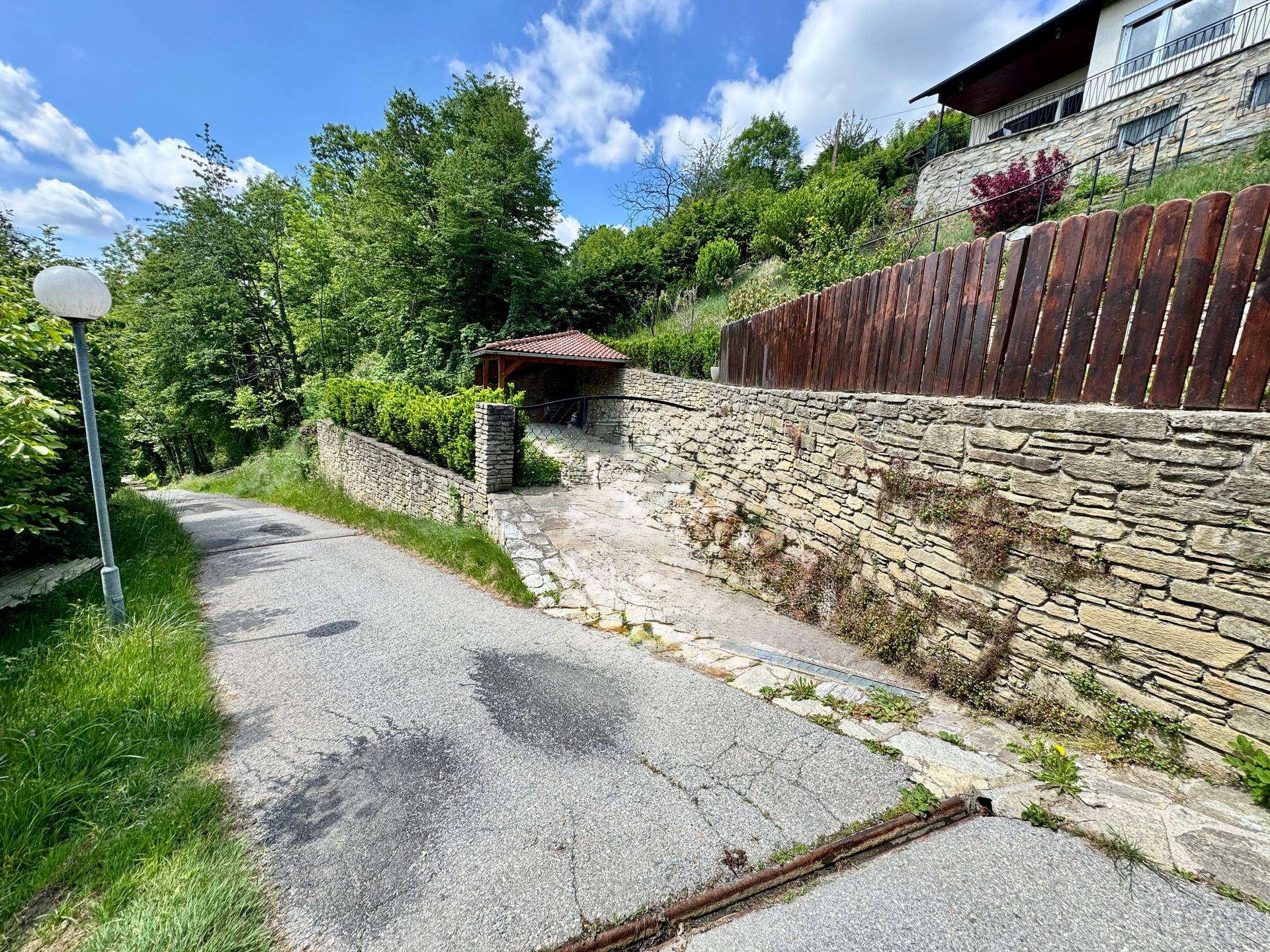 Zufahrtsweg zum Anwesen mit Steinmauern und überdachtem Stellplatz, eingebettet in die Natur.