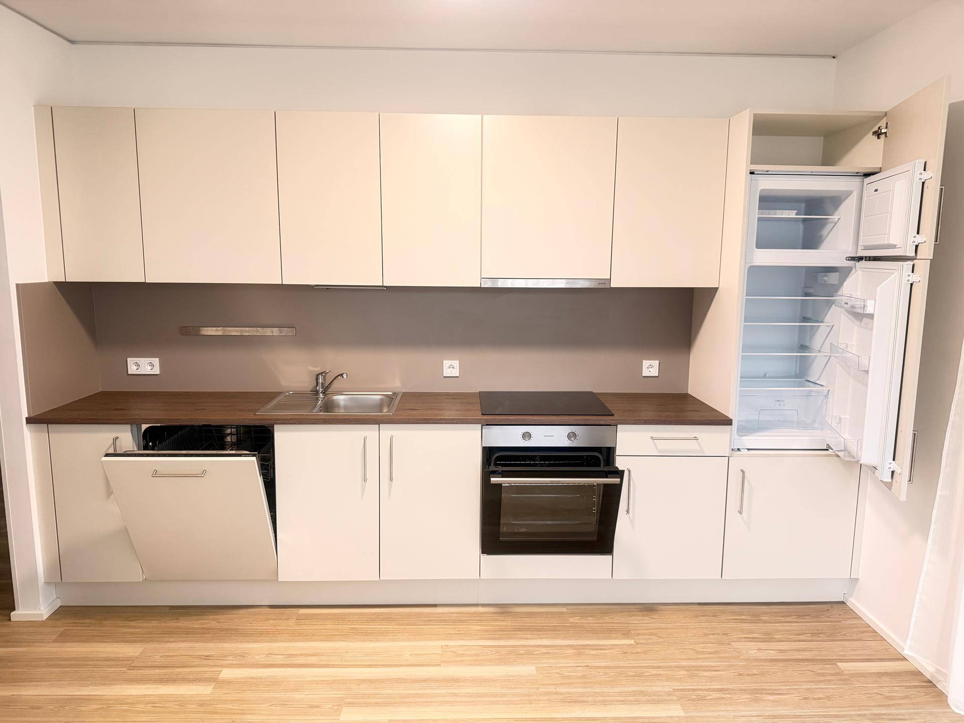 Voll ausgestattete Einbauküche mit hellen Fronten, Kühlschrank und Geschirrspüler.