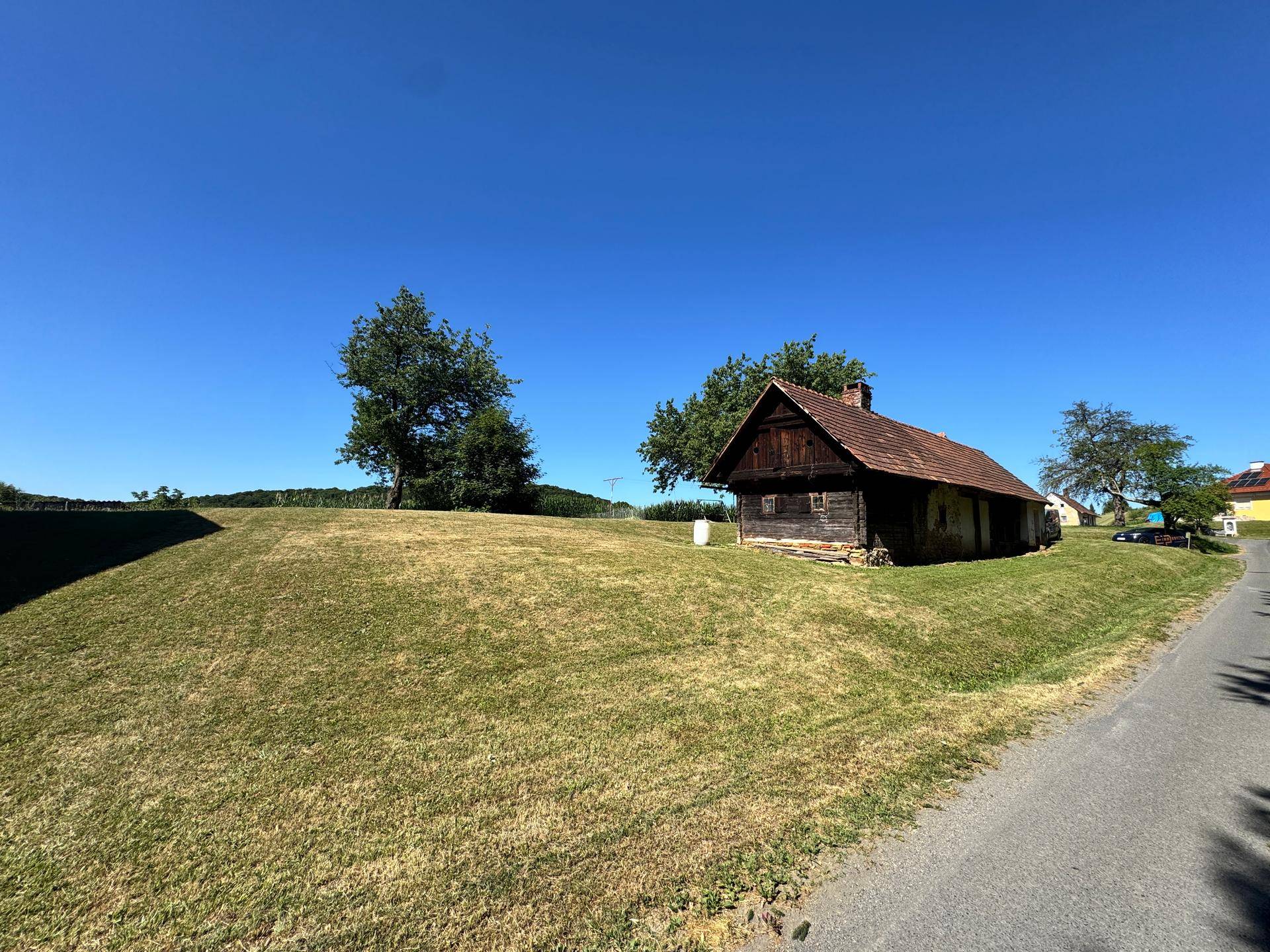 Rustikales Holzhaus auf einem grünen Hügel neben einer Landstraße unter blauem Himmel.