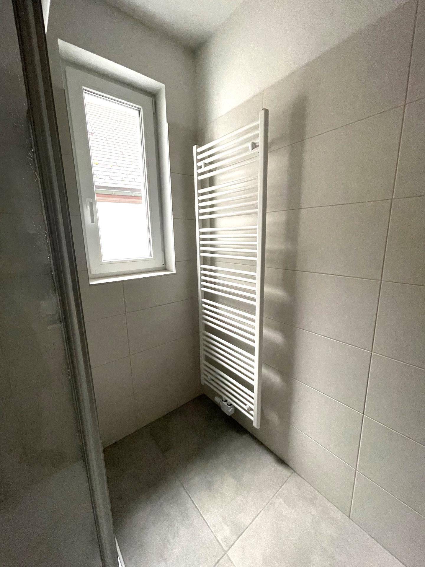 Modernes Badezimmer mit Fenster, Handtuchheizkörper und hellen Wandfliesen, bietet Komfort und Stil.