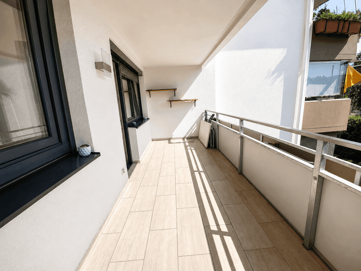 Heller Balkon mit Fliesenboden und Metallgeländer, ideal für sonnige Stunden.
