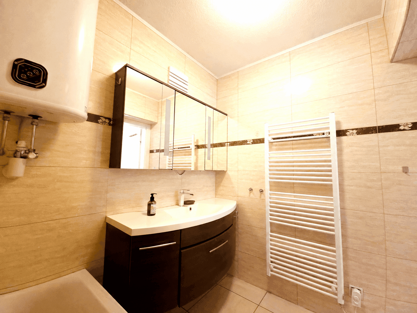 Badezimmer mit beigefarbenen Fliesen, Waschbeckenunterschrank und beheiztem Handtuchhalter.