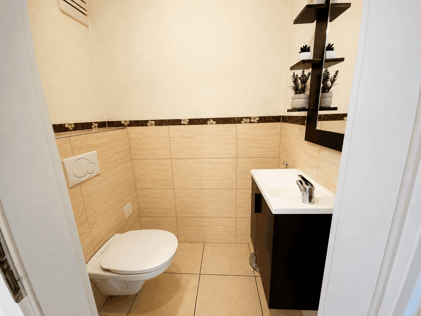 Kleines Gäste-WC mit Wand-WC, Waschbecken und beigefarbenen Fliesen.