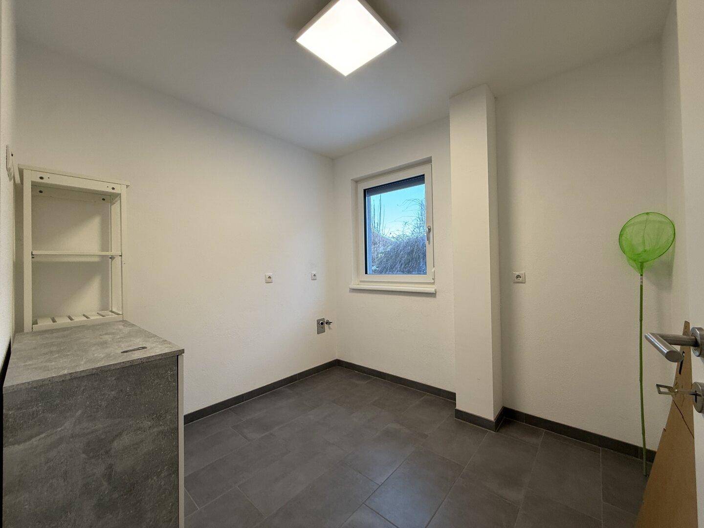 Praktischer Hauswirtschaftsraum mit Fenster, gefliestem Boden und Anschlüssen für Waschmaschine.