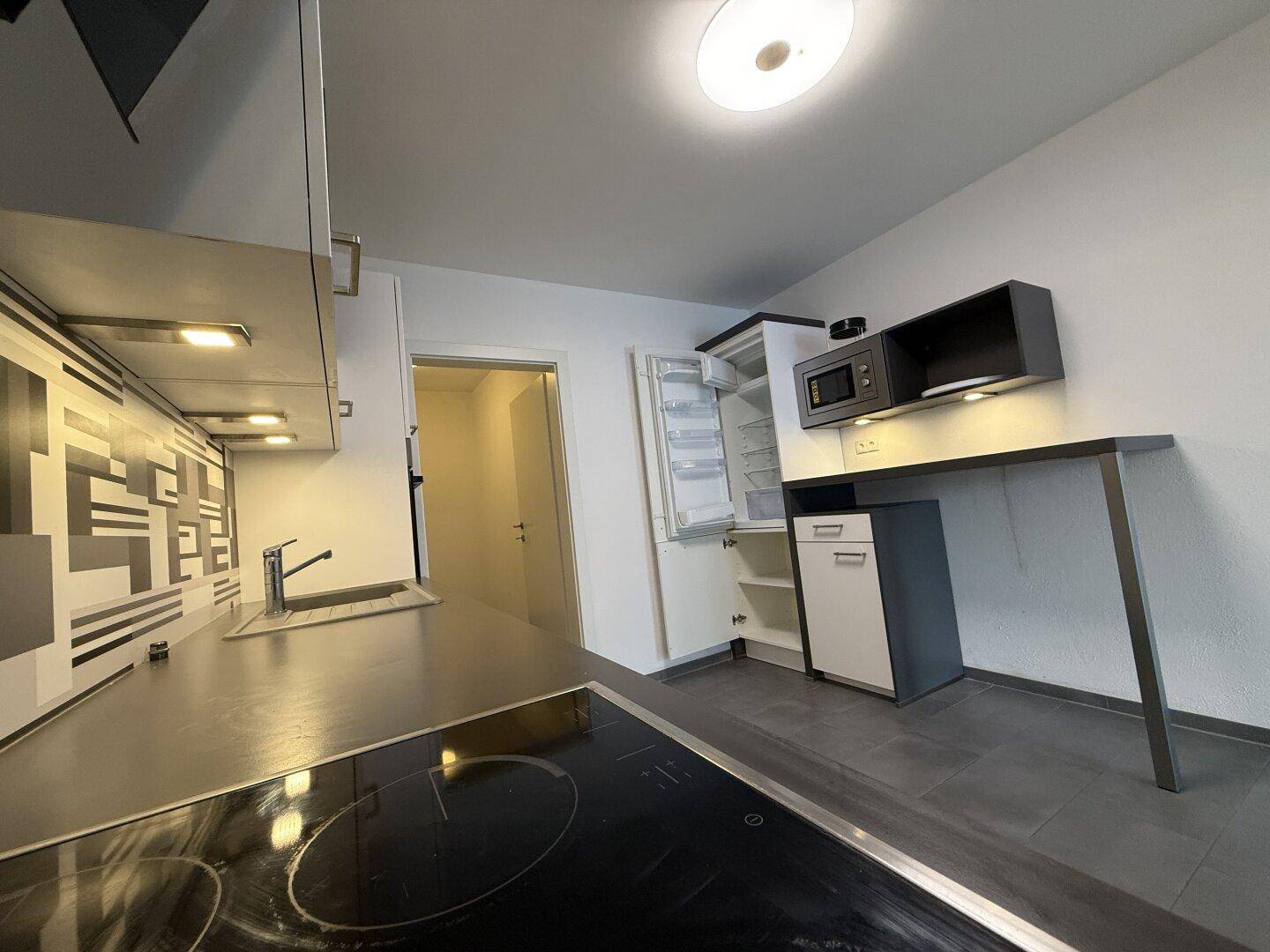 Funktionale Küche mit Induktionskochfeld, Spüle und integriertem Kühlschrank, ideal für den täglichen Gebrauch.