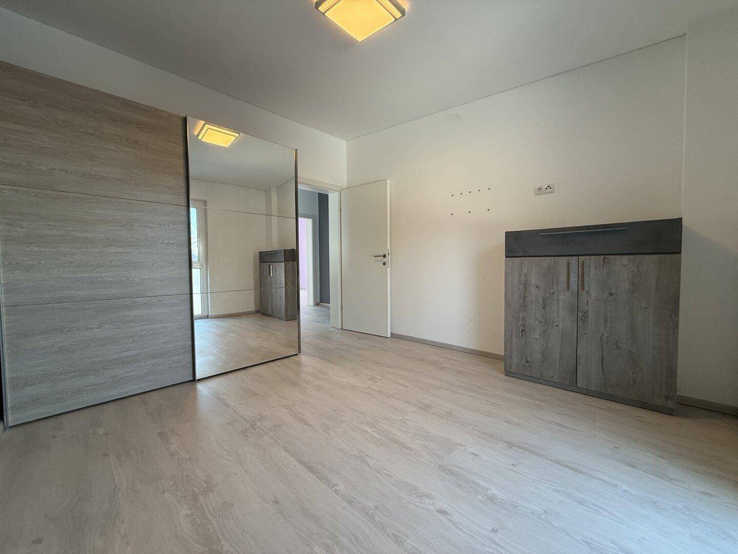 Schlafzimmer mit hellem Laminatboden und großem Spiegelschrank, der den Raum optisch vergrößert.