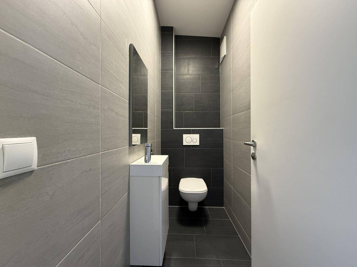 Modernes Gäste-WC mit dunklen Fliesen, Wand-WC und kleinem Waschbecken.