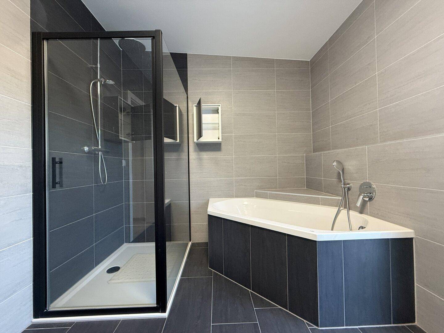 Modernes Badezimmer mit Duschkabine, Eckbadewanne und eleganten grauen Fliesen.