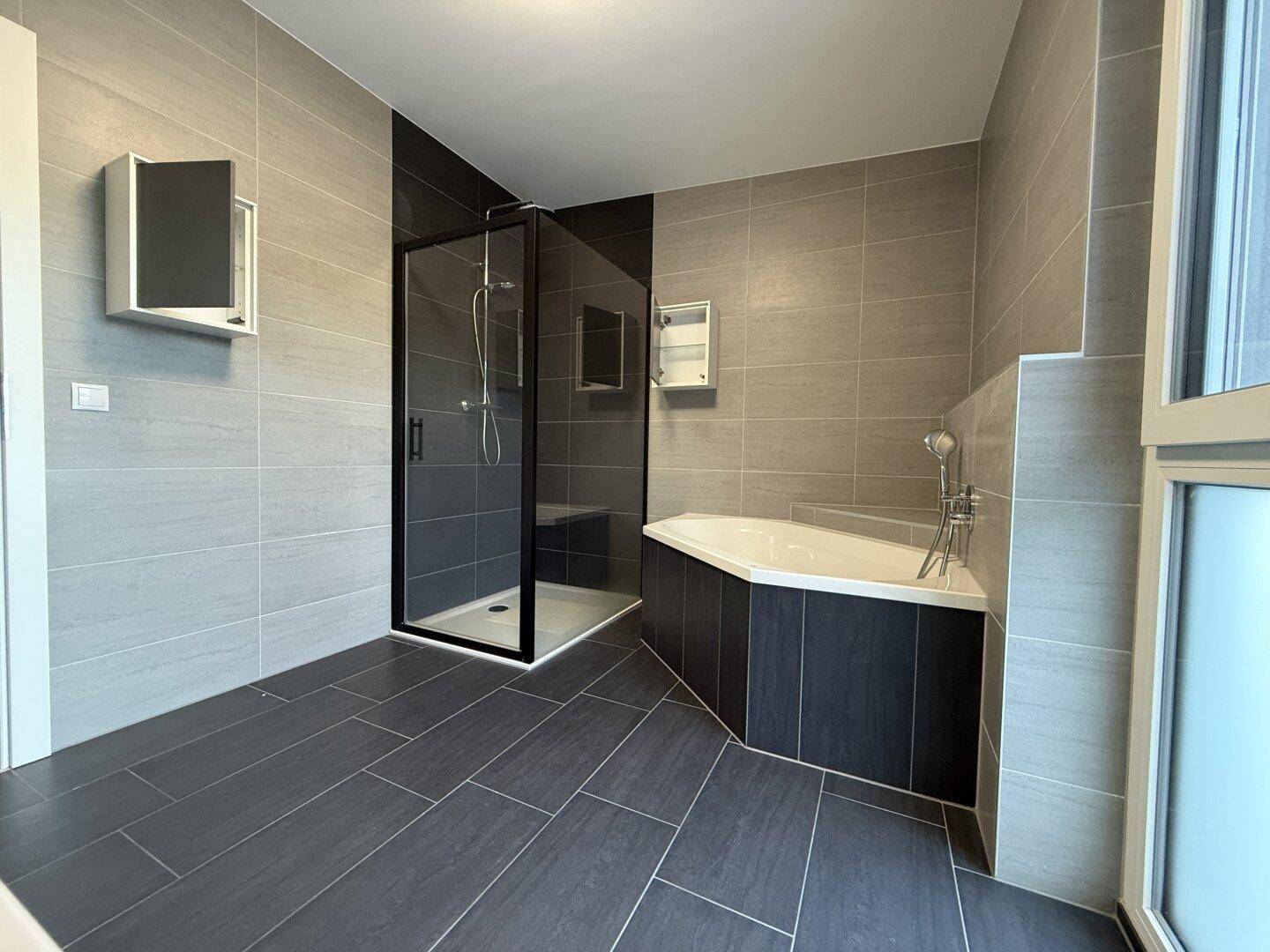 Helles Badezimmer mit Duschkabine, Eckbadewanne und großem Fenster für viel Tageslicht.