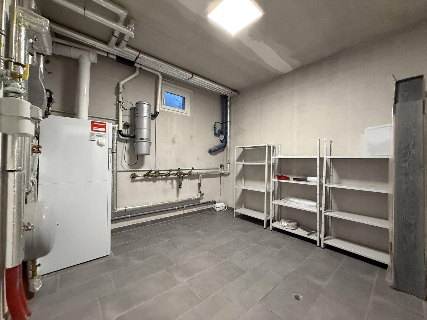 Technikraum im Keller mit Heizungsanlage, Rohren und Regalen für zusätzlichen Stauraum.