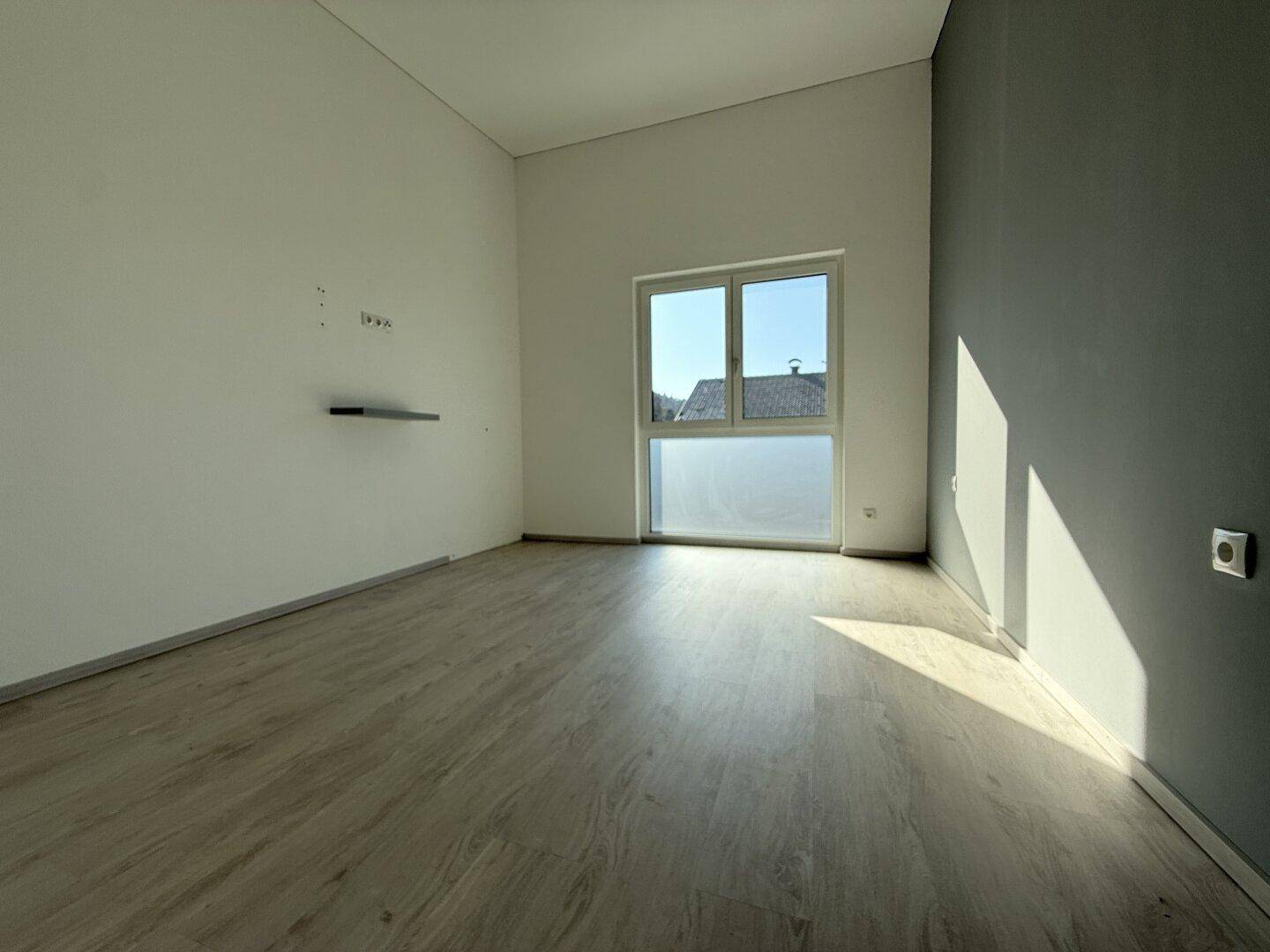 Geräumiges Schlafzimmer mit hellem Laminatboden und großem Fenster, das viel Tageslicht hereinlässt.
