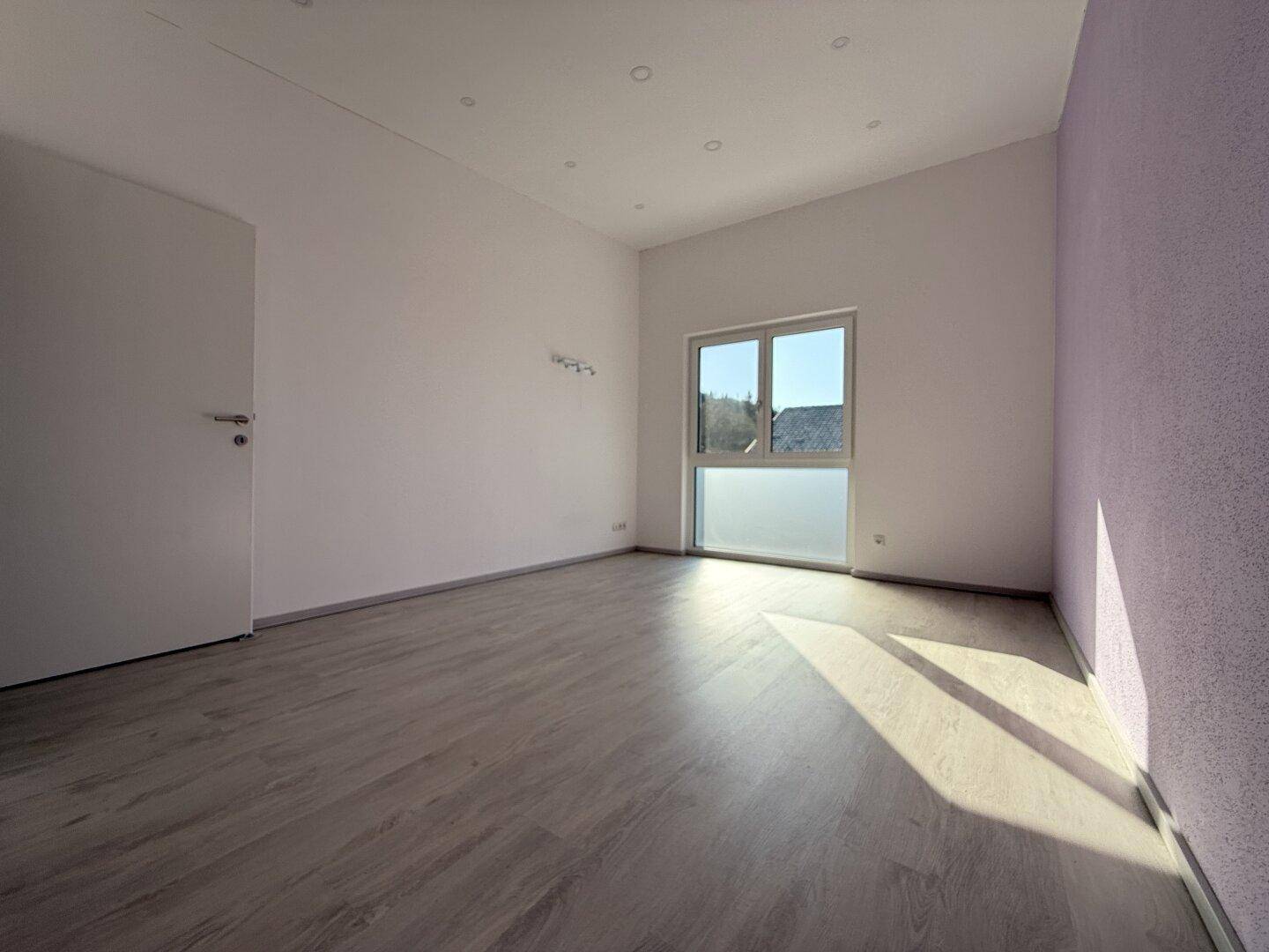 Helles Schlafzimmer mit Laminatboden, weiß gestrichenen Wänden und einem großen Fenster.
