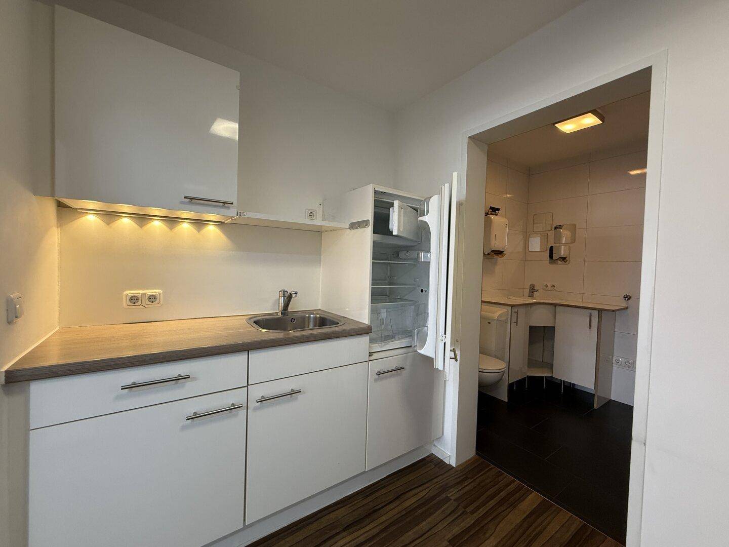 Kleine, funktionale Küchenzeile mit integriertem Kühlschrank und Blick auf den Sanitärbereich.