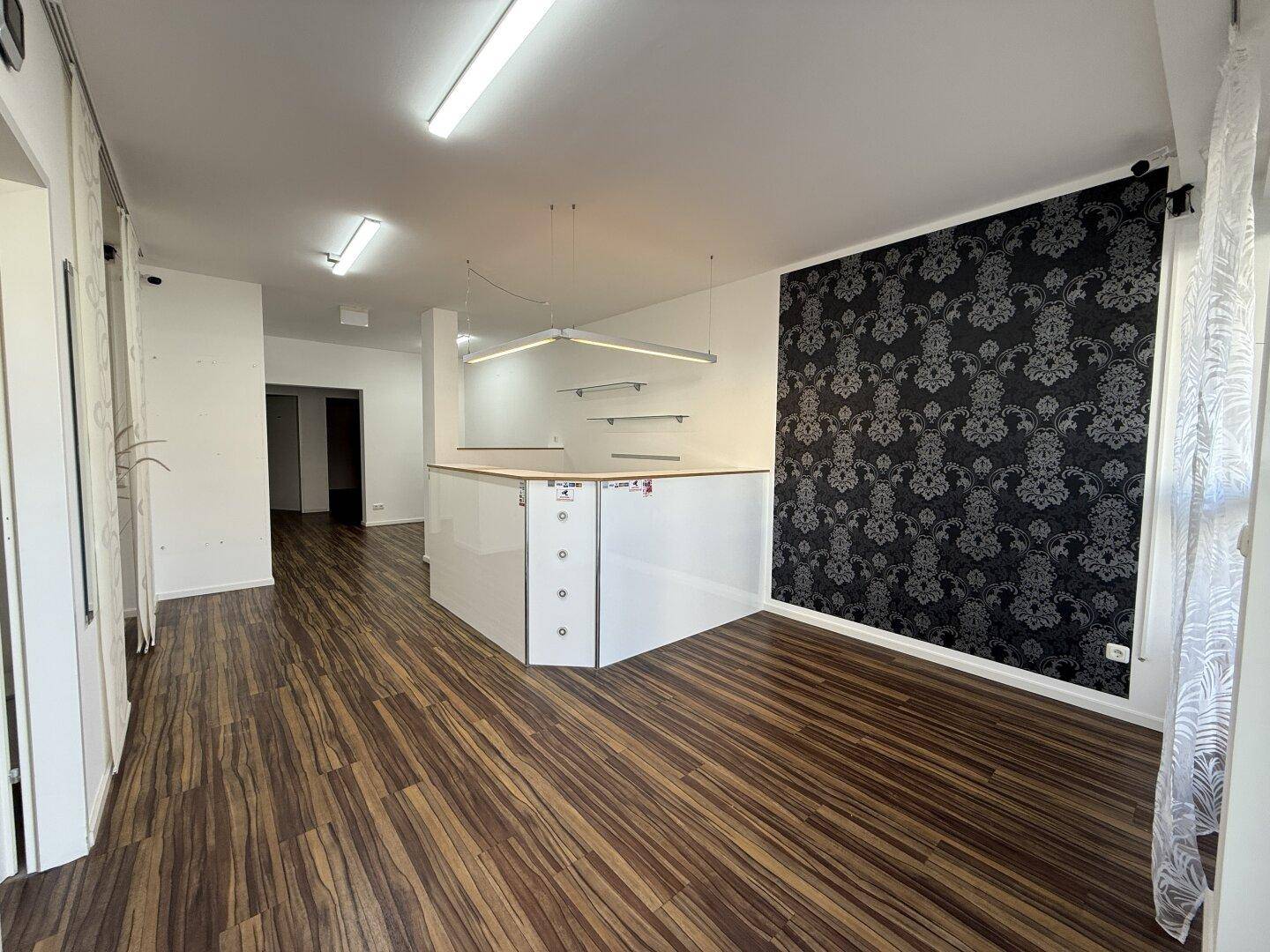 Geräumiger Empfangsbereich mit dunklem Laminatboden, einer Theke und einer auffälligen Tapetenwand.