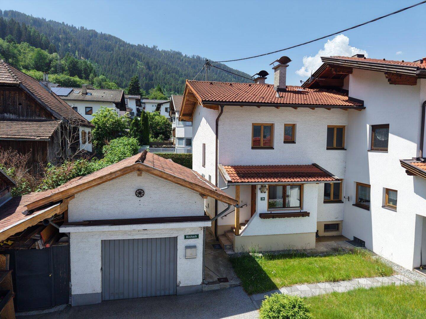 Vorderansicht des Hauses mit Garage, Vorgarten und Blick auf die bewaldeten Berghänge.