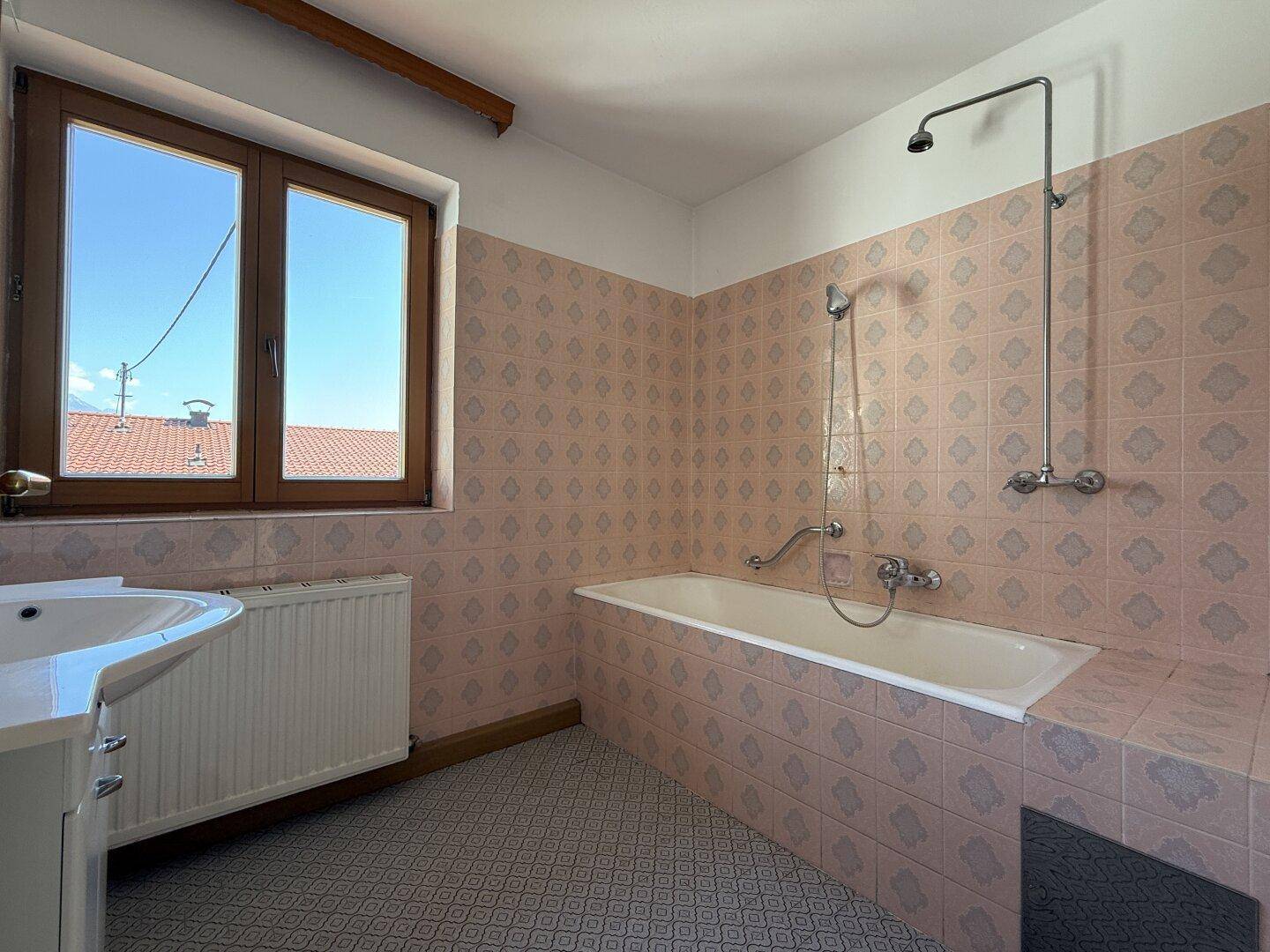 Badezimmer im 80er-Jahre-Stil mit rosa Fliesen, Badewanne und Fenster.