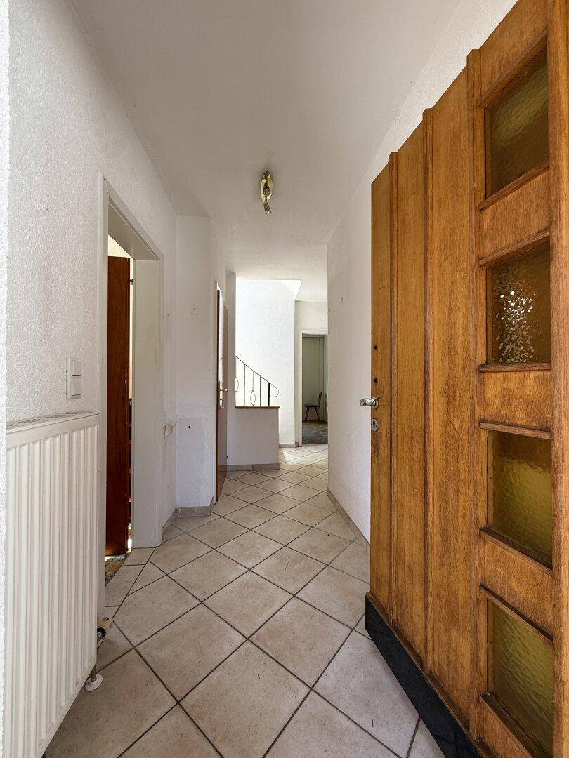 Heller Eingangsbereich mit Fliesenboden und einer Holztür mit Glaseinsätzen.