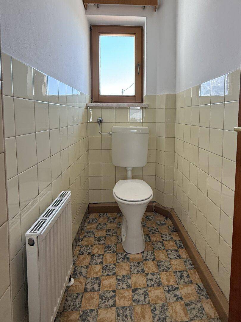 Separate Toilette mit Fenster, WC und gefliesten Wänden in hellem Farbton.