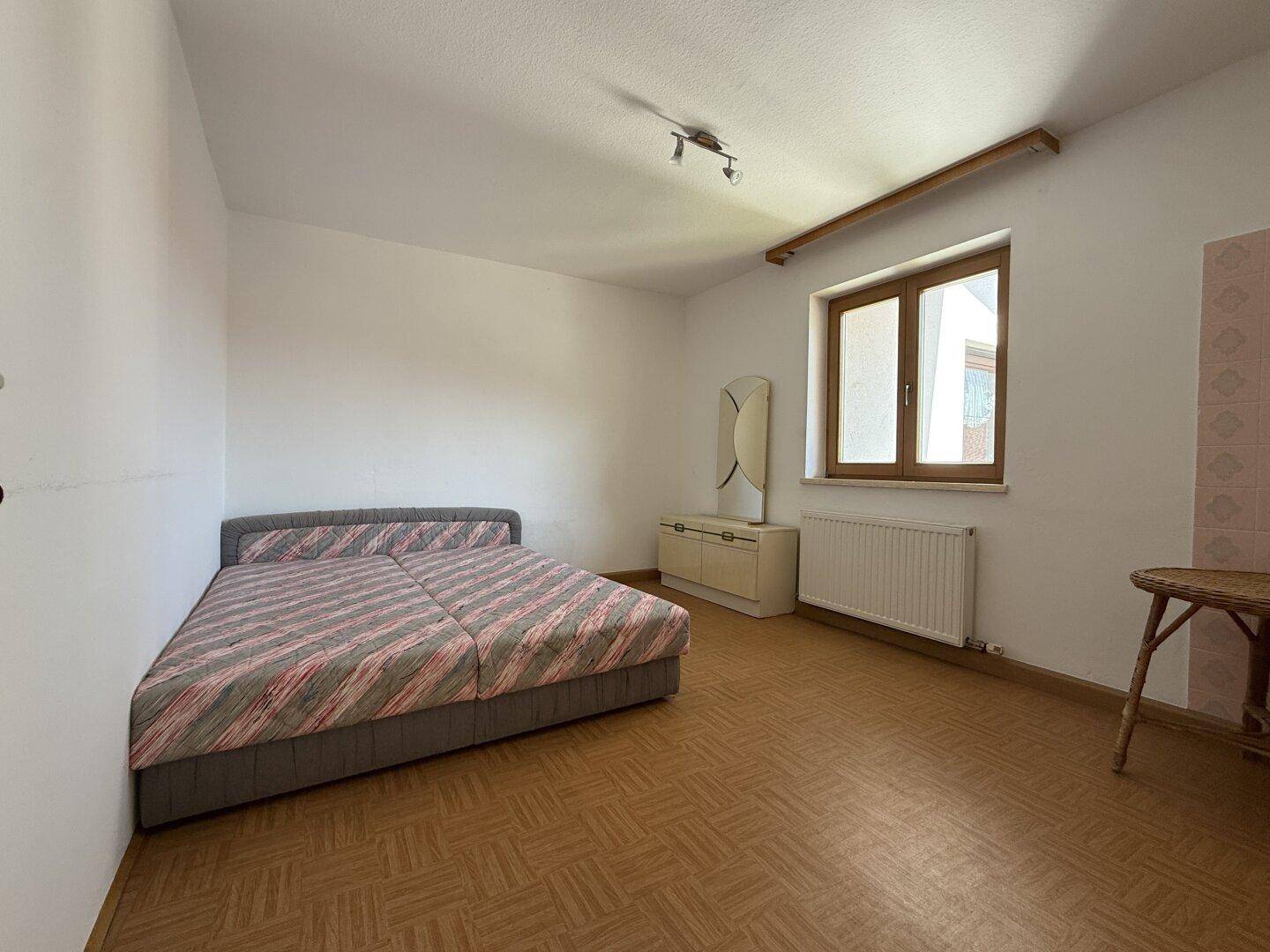 Schlafzimmer mit Parkettboden, Doppelbett und Fenster mit Blick auf die Umgebung.