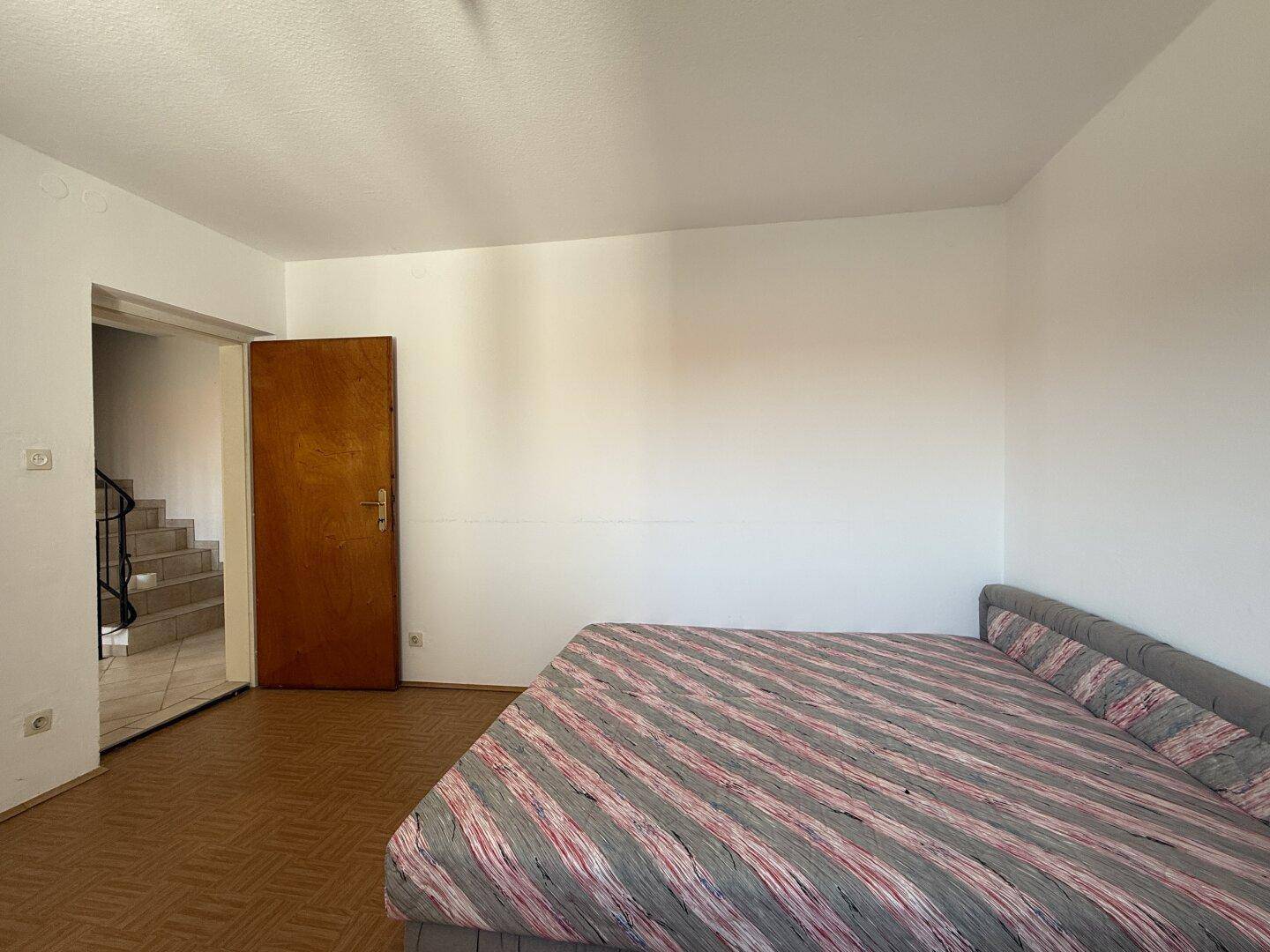 Schlafzimmer mit Doppelbett und Zugang zum Flur, hell und einfach eingerichtet.