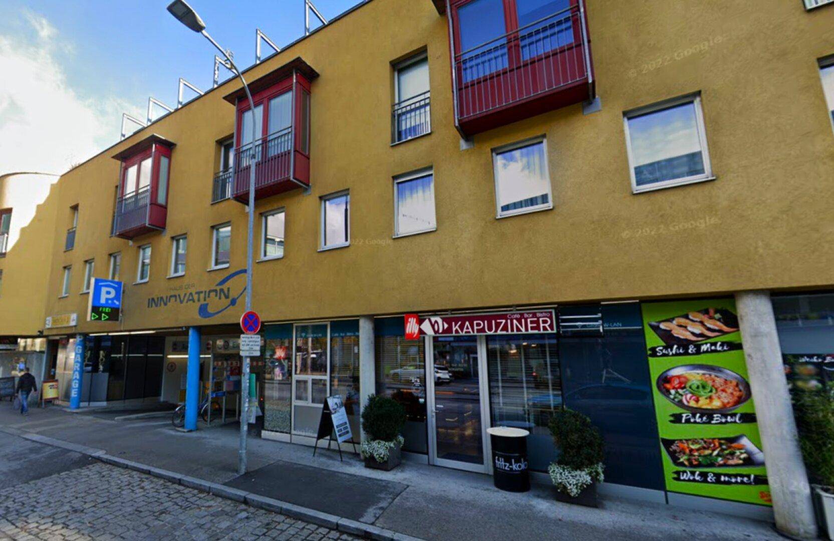 Moderne Gebäudefassade mit Geschäften im Erdgeschoss und Wohnungen mit Balkonen darüber.