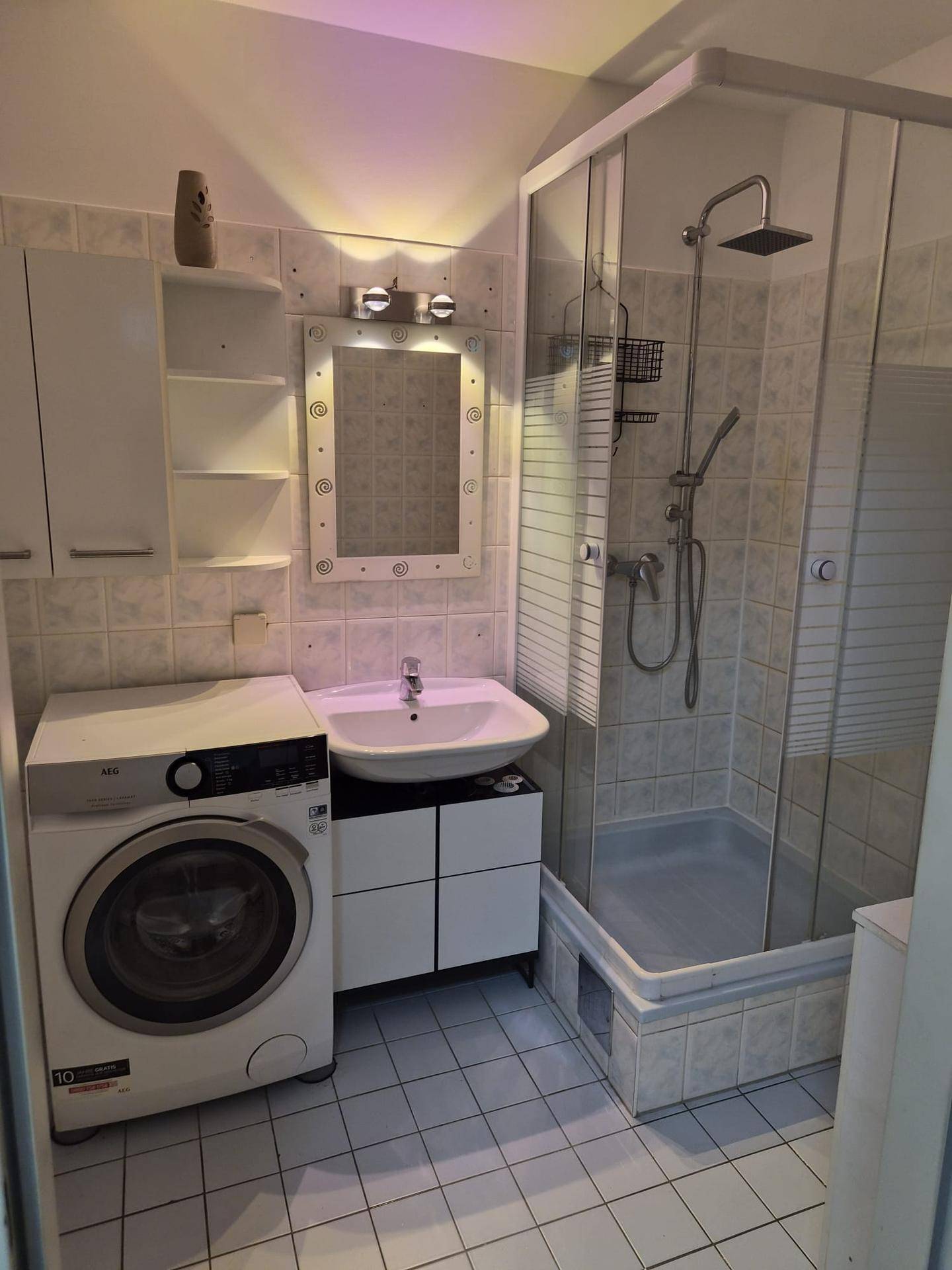 Komplettes Badezimmer mit Duschkabine, Waschbecken, Spiegel und Waschmaschine.
