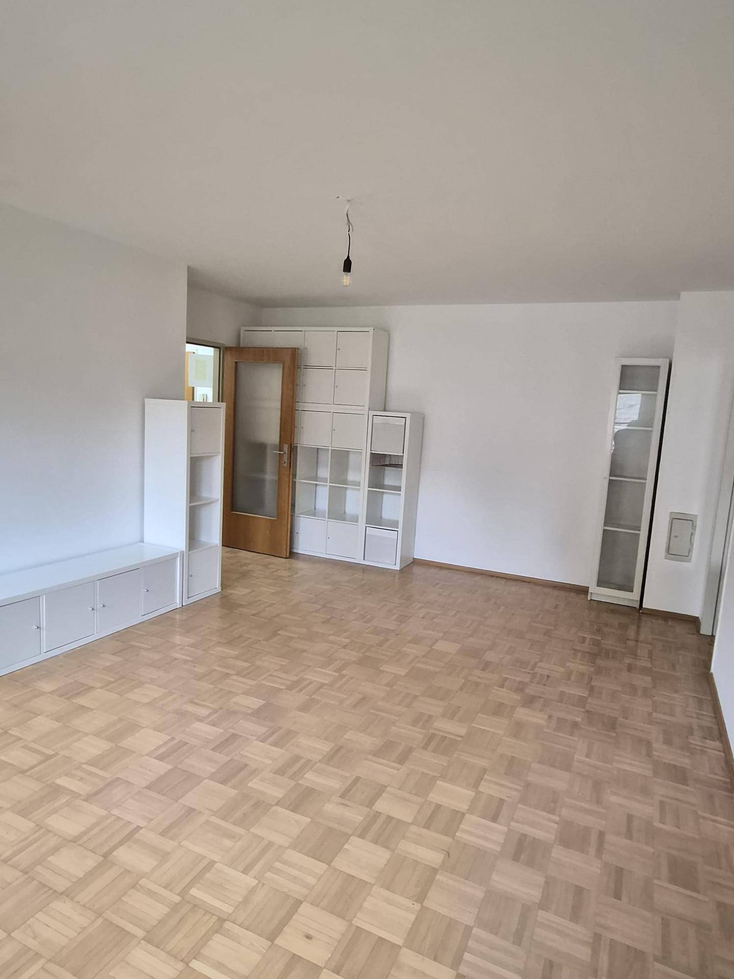 Geräumiges Wohnzimmer mit Parkettboden und modularen weißen Regalsystemen.