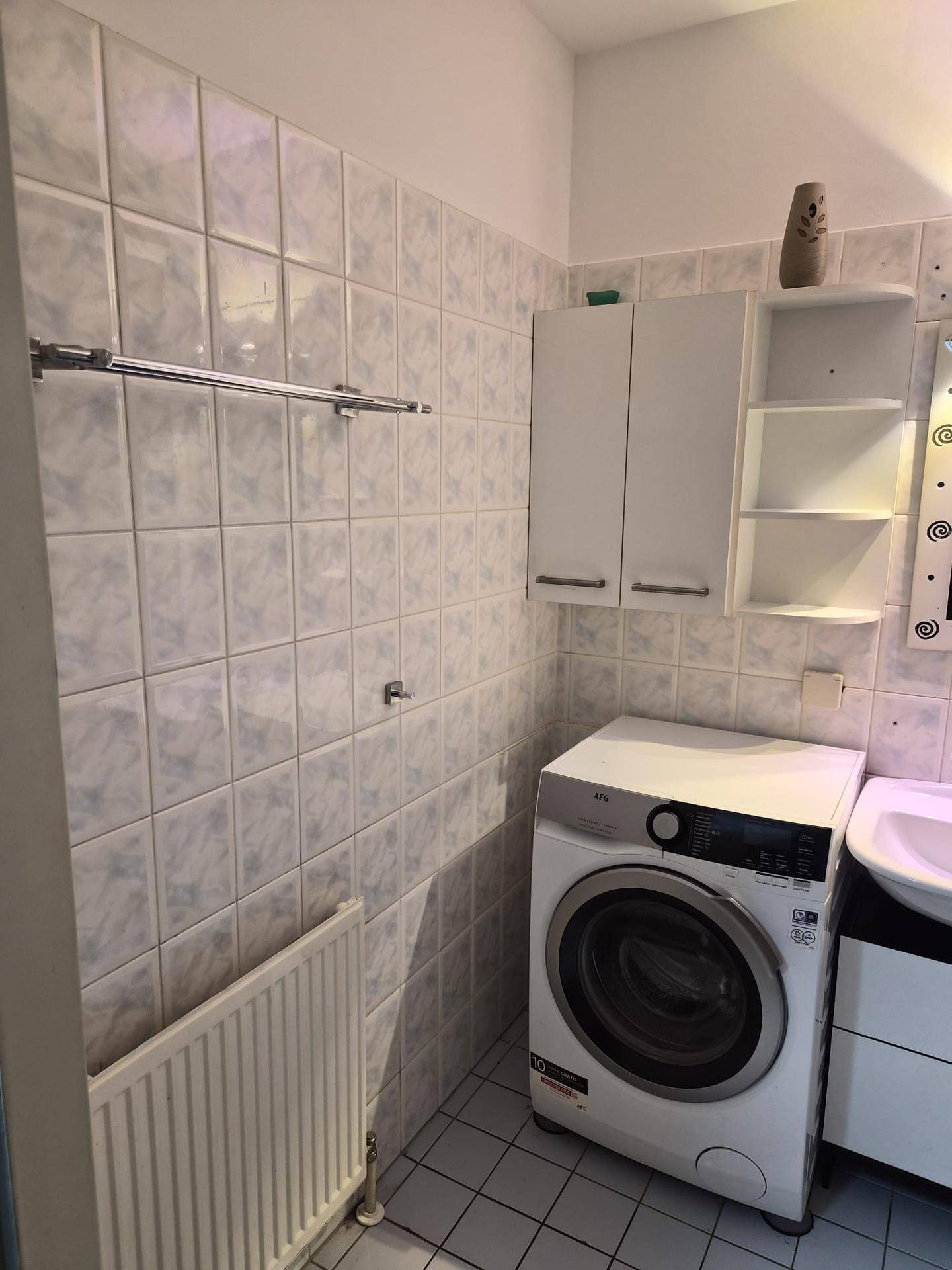Badezimmer mit hellen Fliesen, Waschmaschine und Handtuchhalter.