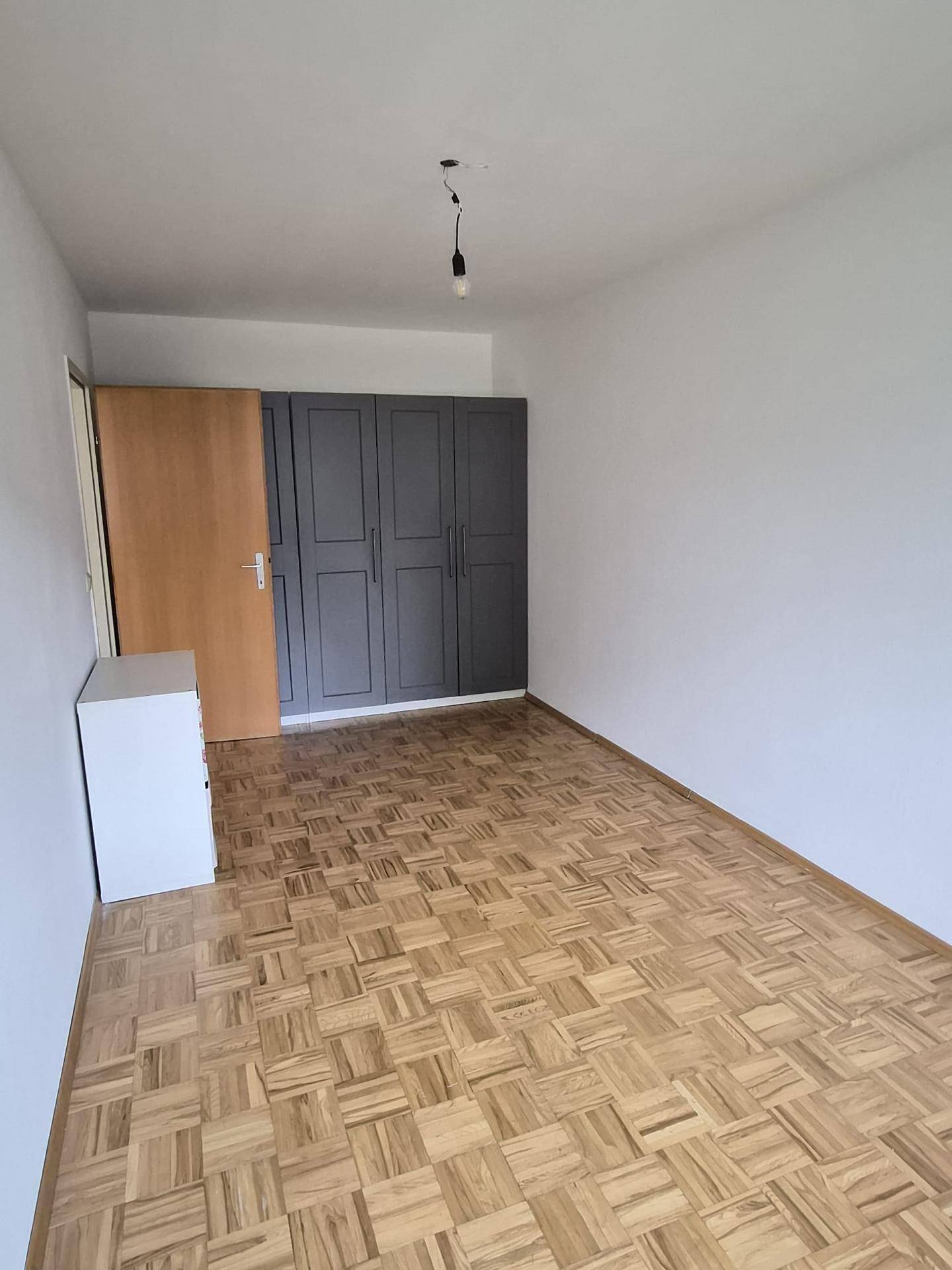 Schlafzimmer mit Parkettboden, weißen Wänden und einem praktischen Einbauschrank.