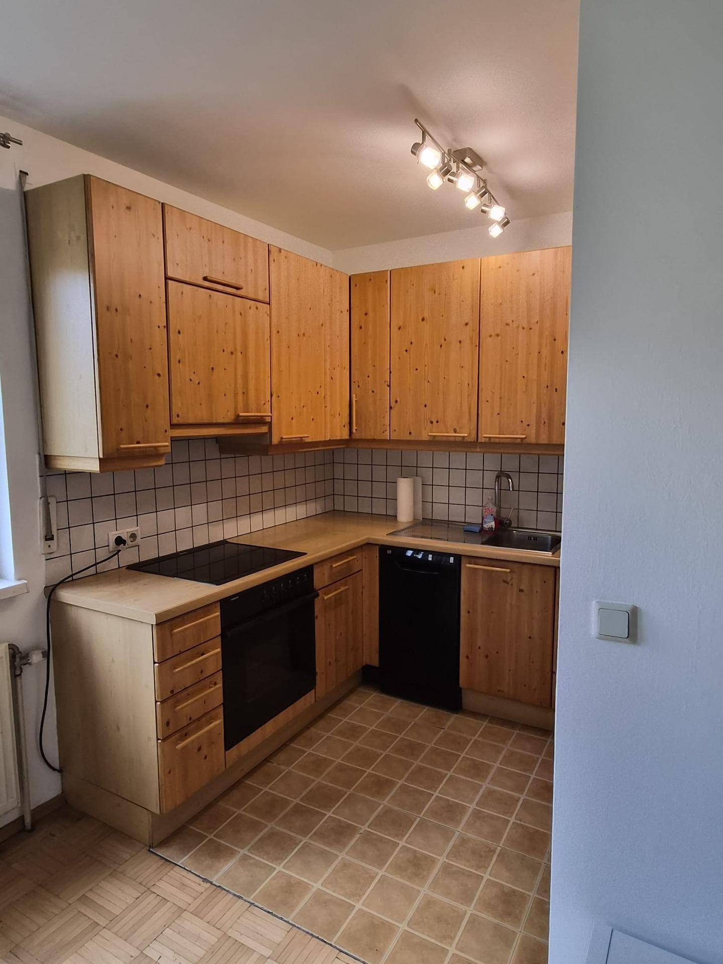 Funktionale Küche mit Holzschränken, weißen Fliesen und integrierten schwarzen Elektrogeräten.