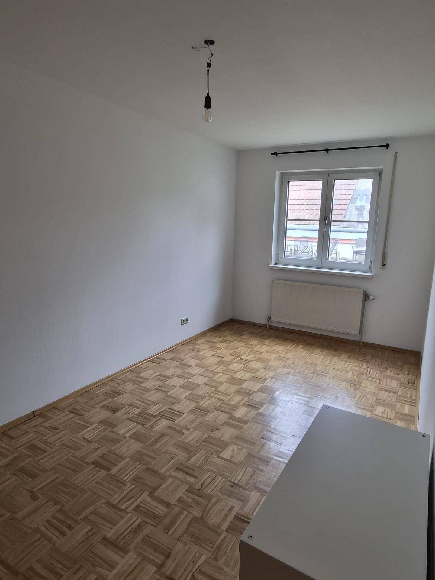 Helles Schlafzimmer mit Parkettboden, Fenster und Heizkörper, bereit zur individuellen Gestaltung.