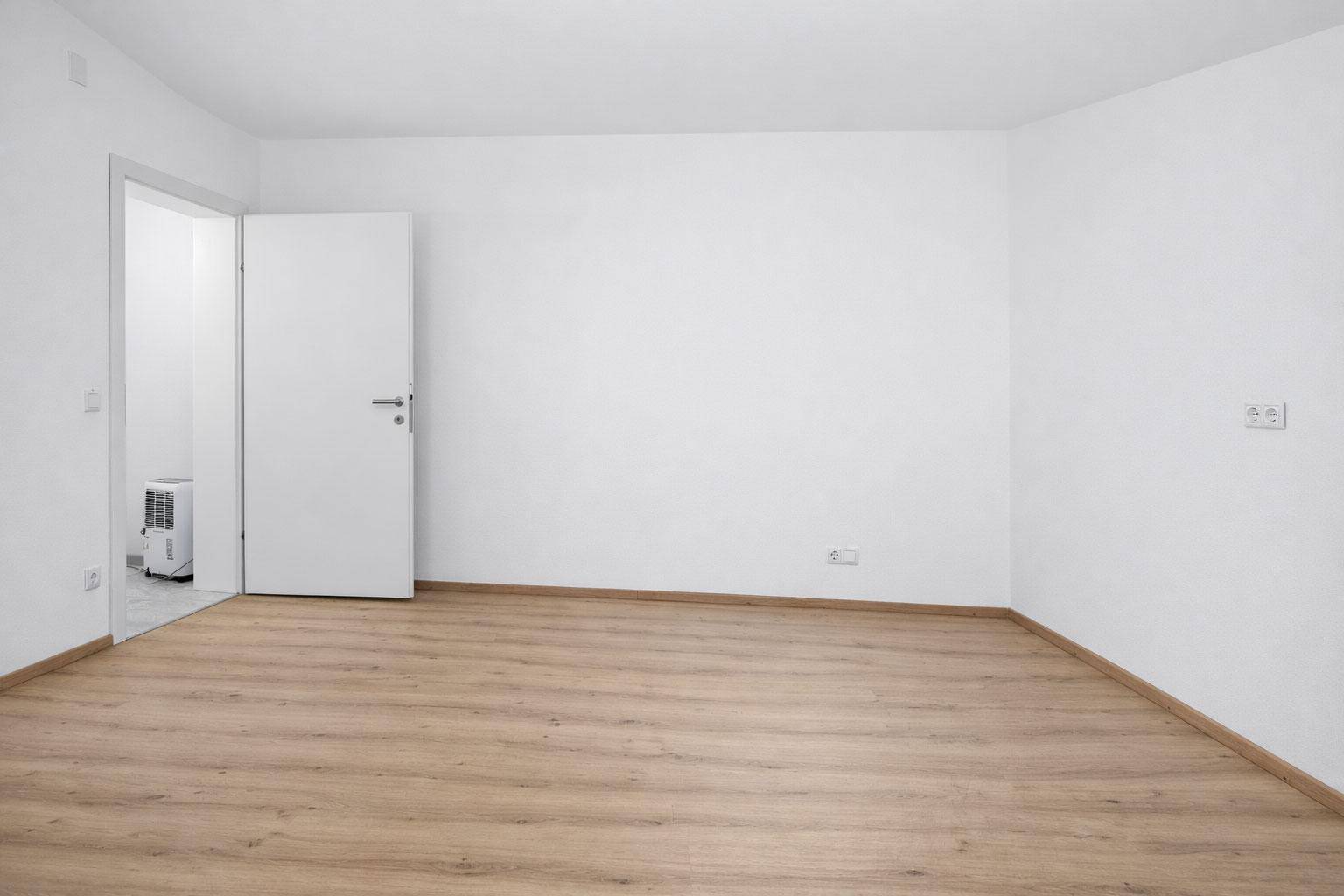 Helles, leeres Zimmer mit Laminatboden und weiß gestrichenen Wänden, ideal für Schlafzimmer.