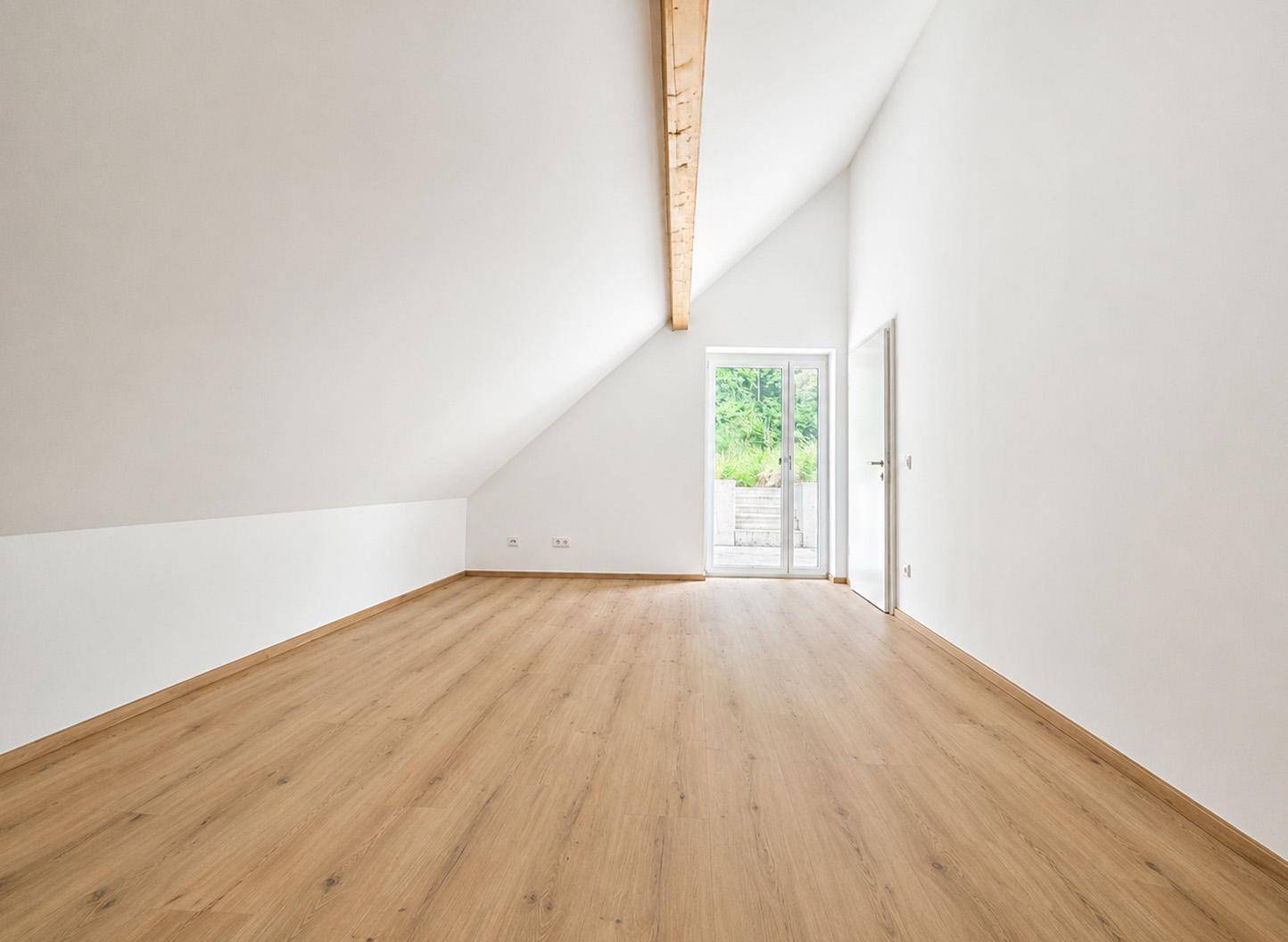 Helles, leeres Zimmer im Dachgeschoss mit Laminatboden und Zugang nach draußen.
