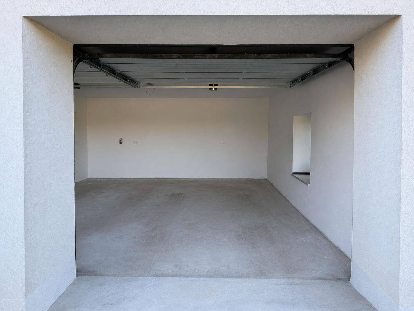 Leere Garage mit Betonboden, hellen Wänden und einem schmalen Fenster, bereit zur Nutzung.