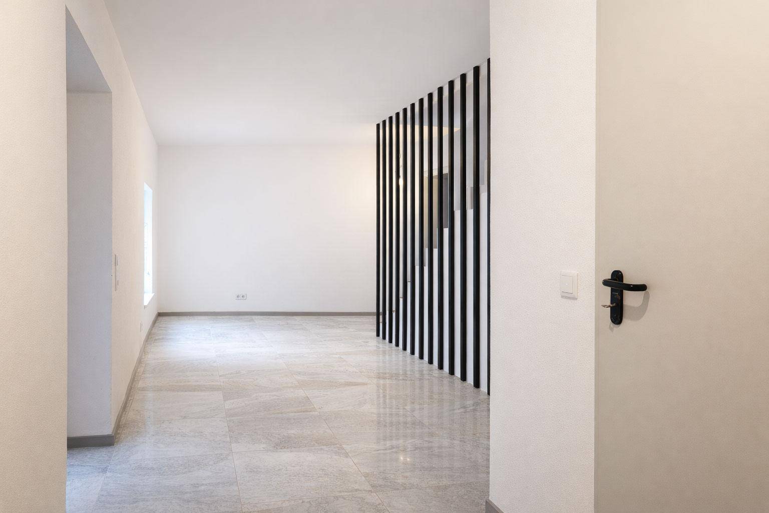 Heller, leerer Raum mit modernen Fliesen und einer dekorativen schwarzen Lamellenwand.