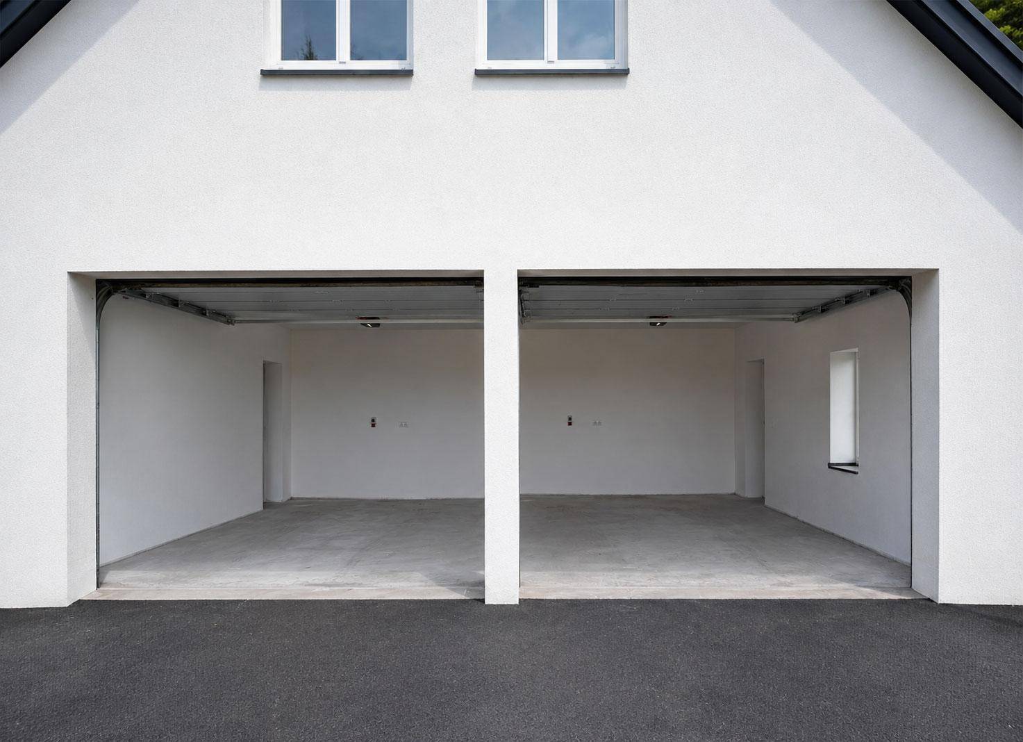 Doppelgarage mit zwei offenen Toren, leeren Betonböden und weißer Fassade des Hauses.