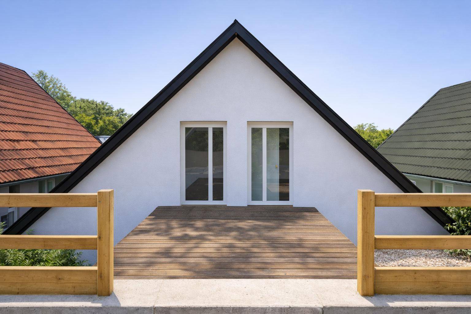 Moderne Hausfassade mit weißem Putz, schwarzem Satteldach und einer Holzplattform im Obergeschoss.